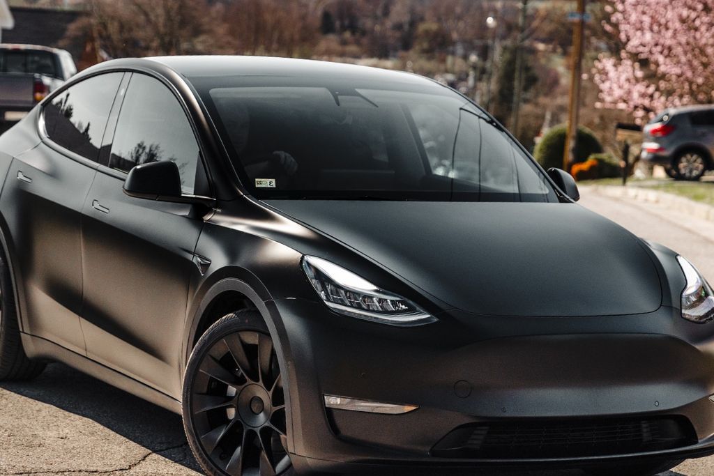 A blacked-out Tesla Model Y with a matte finish and dark ceramic window tint parked on a suburban street. The deep tint enhances privacy while offering superior heat rejection and UV protection. The sleek, modern design showcases the premium quality of ceramic tinting.