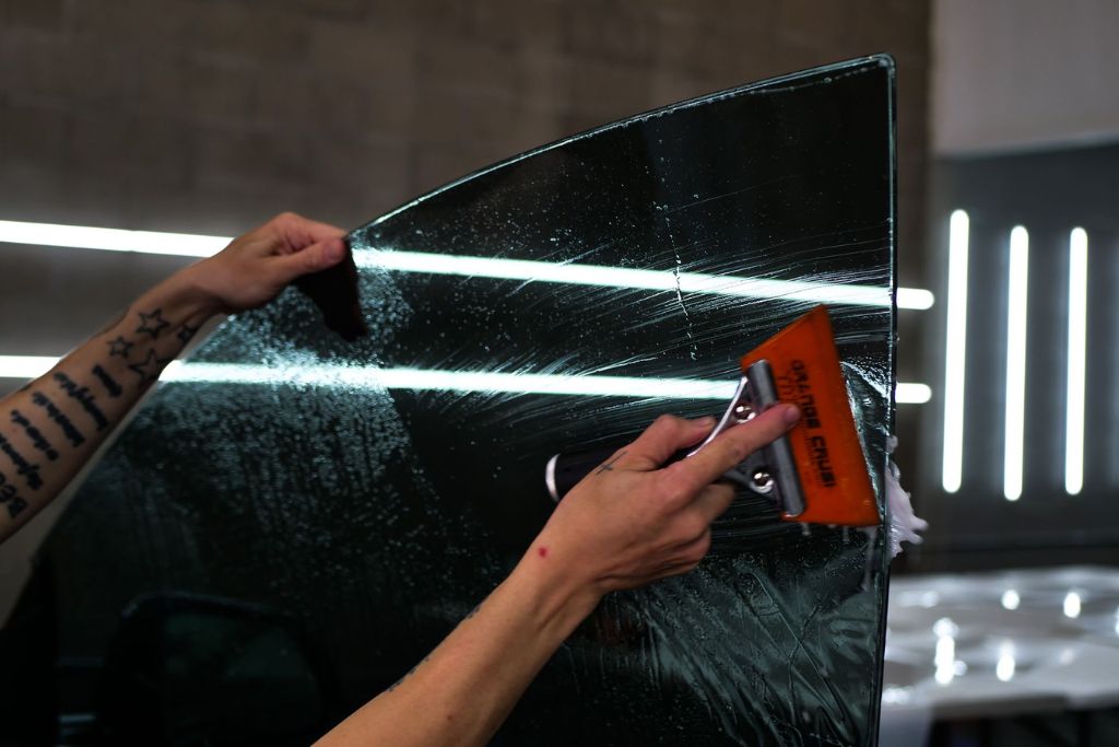 Technician applying window tint film to a car window using a squeegee, demonstrating the added benefits of heat, glare, and UV protection.