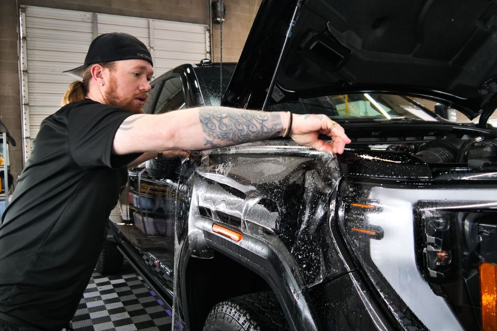A technician installs Paint Protection Film (PPF) on the fender of a black truck, carefully aligning and smoothing the transparent film along the edge. This image helps illustrate Common Concerns About PPF, such as installation quality, film visibility, and long-term durability.