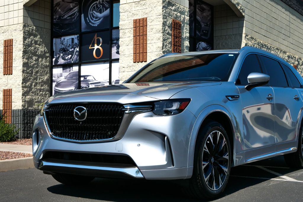 Silver Mazda SUV with tinted windows parked outside a detailing shop, representing the benefits of UV-blocking car tints for skin and interior protection.