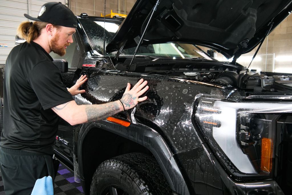 Detailing professional applying paint protection film to a black truck fender, illustrating the drawbacks and limitations of PPF such as higher cost, need for expert installation, potential yellowing, required maintenance, and limited impact resistance.