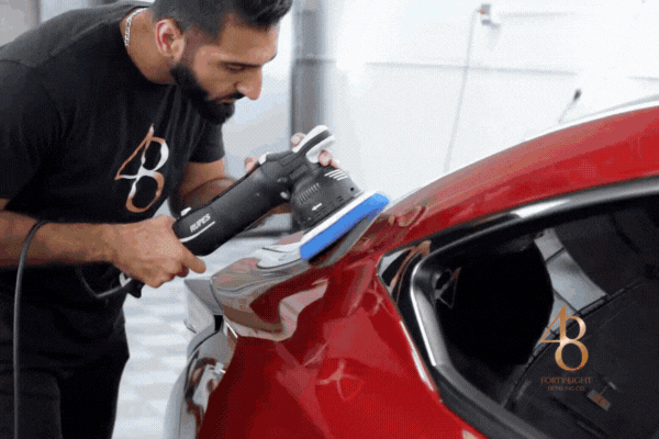 Detailer applying high-performance ceramic coating to a red sports car with a polishing machine, enhancing gloss and adding long-lasting hydrophobic protection.