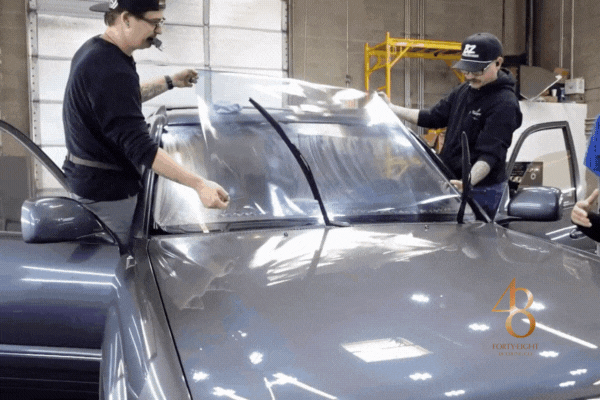 Two professional installers applying a precision-cut UV-blocking window tint film to a car windshield, ensuring smooth coverage and long-lasting heat reduction.