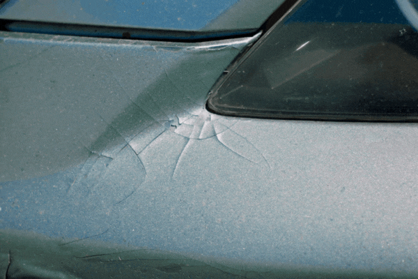 Close-up of cracked and chipped car paint near the rear window, showing damage from rock chips that can lead to rust and reduced vehicle value.