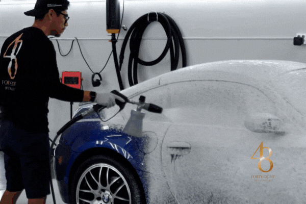 Professional detailer applying thick foam to a blue BMW sports car, showcasing expert maintenance that protects paint from bird droppings and other contaminants.