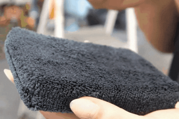 Close-up of hands holding a black microfiber applicator pad soaked with ceramic coating solution, demonstrating professional application techniques that enhance ceramic coating durability.