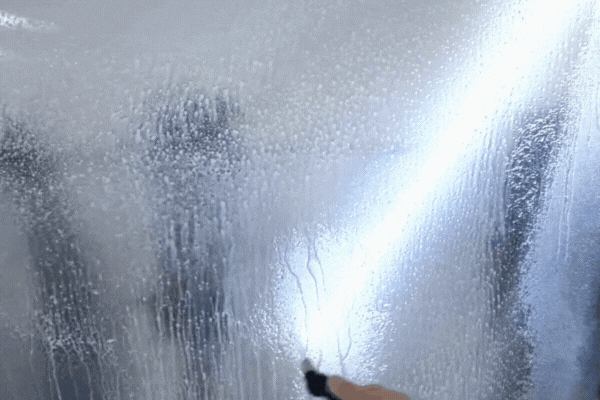 A hand uses a squeegee to smooth out Paint Protection Film (PPF) during installation on a car’s hood, with water droplets visible on the transparent surface. This close-up image answers “What Is PPF on a Car?” by showing the application process of the protective, nearly invisible film.