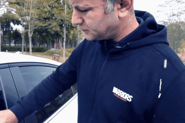 Man inspecting fresh bird droppings on the door of his white car, showing the need to protect your car from bird droppings to avoid acidic paint damage.