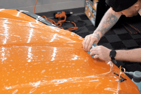 Professional installer applying paint protection film to the hood of an orange car in Surprise Arizona using precision tools to ensure a flawless finish.