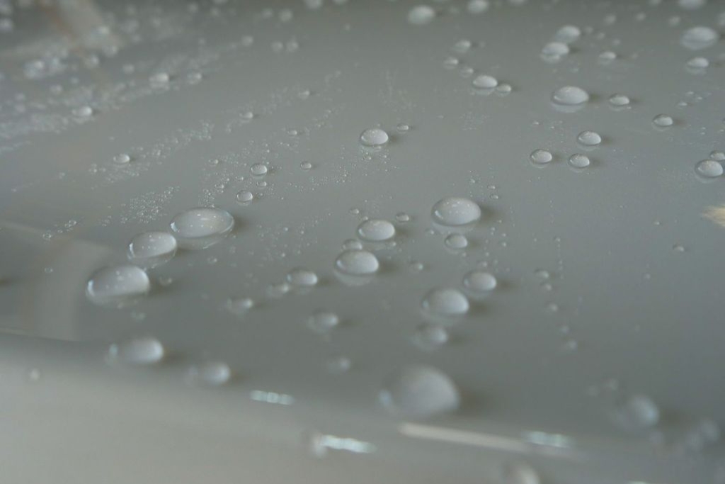 Close-up of water beads on a light-colored ceramic-coated car panel in Surprise, Arizona, visually explaining What Ceramic Coating Actually Does for Water Spots by showing hydrophobic surface behavior