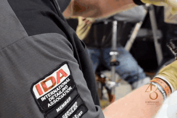 Close-up of a certified detailing expert at 48 Detailing in Surprise, Arizona, applying a ceramic coating while wearing an IDA-certified patch, emphasizing professional care in When Should You Recoat for Maximum Spot Resistance