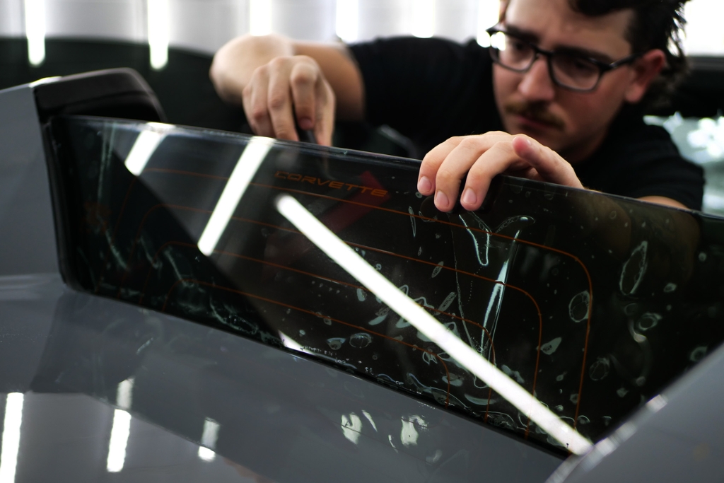 An installer carefully applies ceramic tint to the rear window of a Corvette at 48 Detailing in Surprise Arizona. The image highlights the precision and quality of ceramic tint installation which offers advanced heat and UV protection without sacrificing visibility or signal clarity.