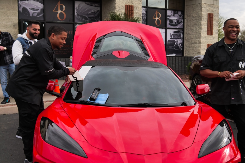A group of installers work on a bright red sports car at 48 Detailing in Surprise Arizona, with a ceramic tint application in progress on the windshield. The image captures a hands-on demonstration of window tinting, aligning with key factors to consider when choosing your tint percentage such as visibility, style, and legal compliance.