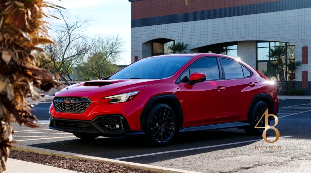 A shiny red Subaru sedan with black wheels and visible window tint parked in a sunny lot outside 48 Detailing in Surprise Arizona. The car's tinted windows reflect the strong desert sun highlighting the importance of selecting the right window tint percentage.