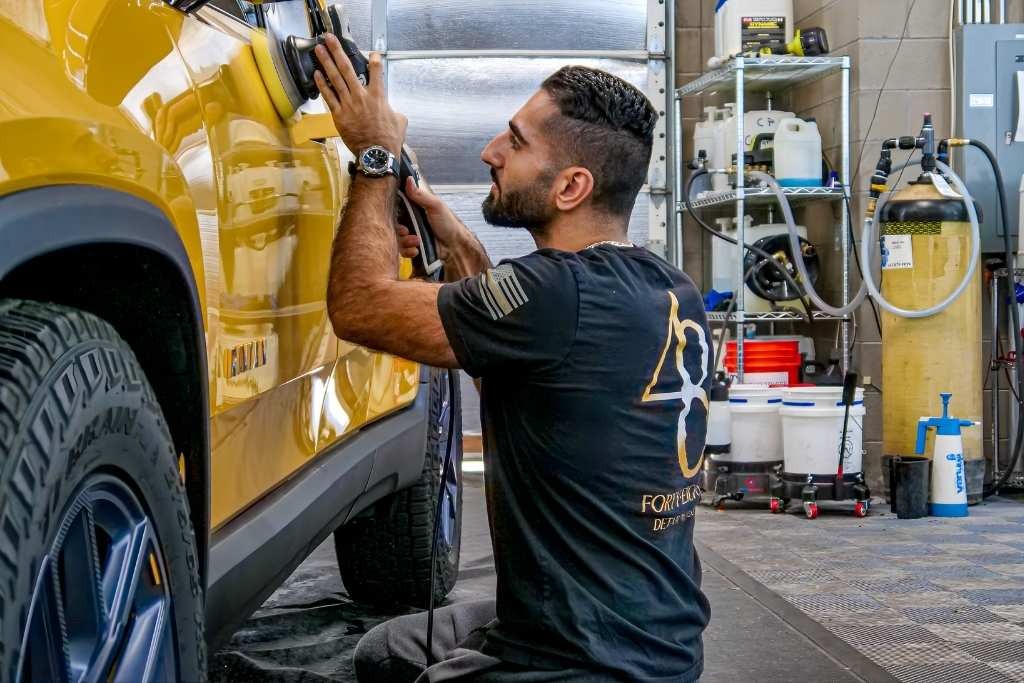 A technician at 48 Detailing in Surprise, AZ applies ceramic coating to a bright yellow SUV inside a detailing bay, illustrating the precision and professional service involved in ceramic coating cost estimates.