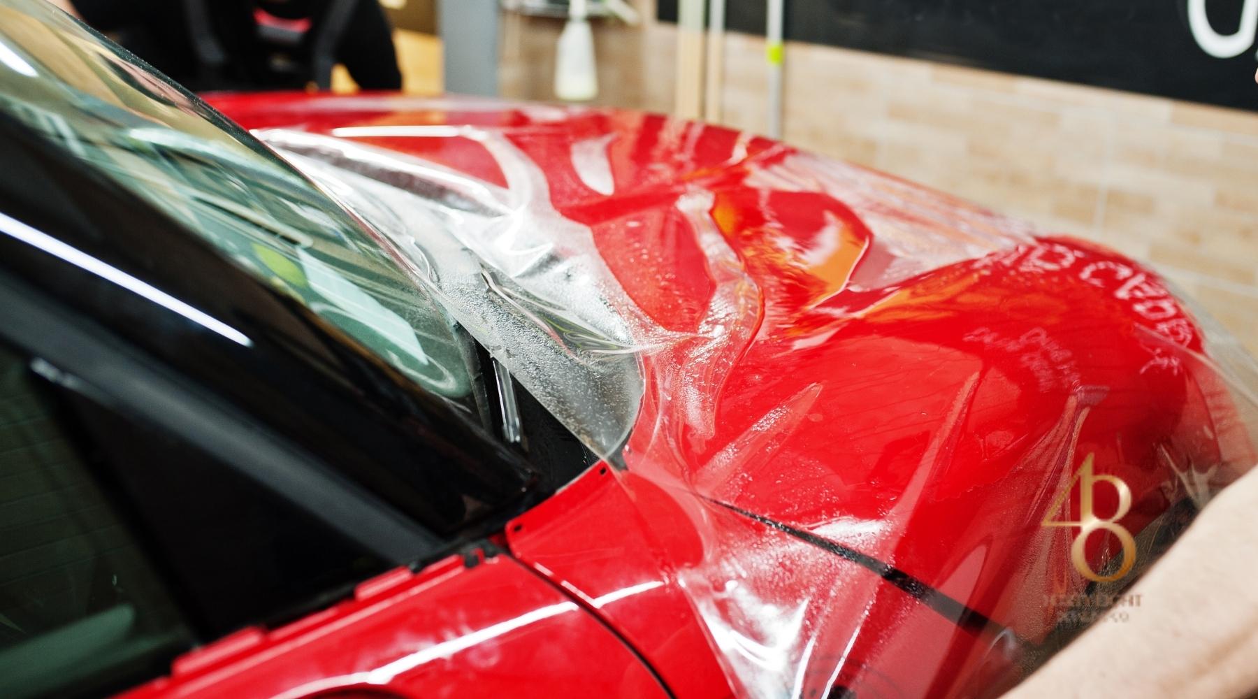 Paint protection film being professionally installed on the hood of a red vehicle at 48 Detailing.