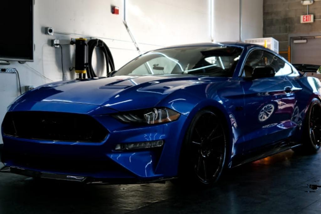Glossy blue muscle car inside a detailing studio, showcasing high-gloss ceramic coating and paint protection film.