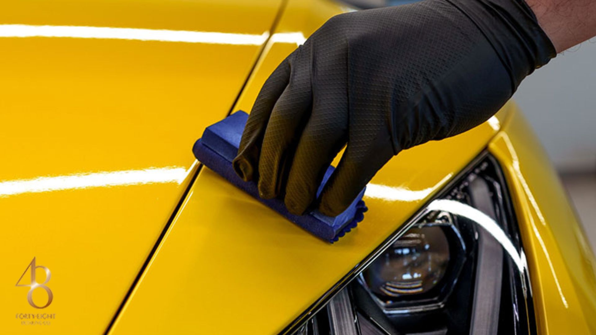 Gloved hand applying ceramic coating to the hood of a yellow car using a foam applicator, highlighting the glossy finish and precision.
