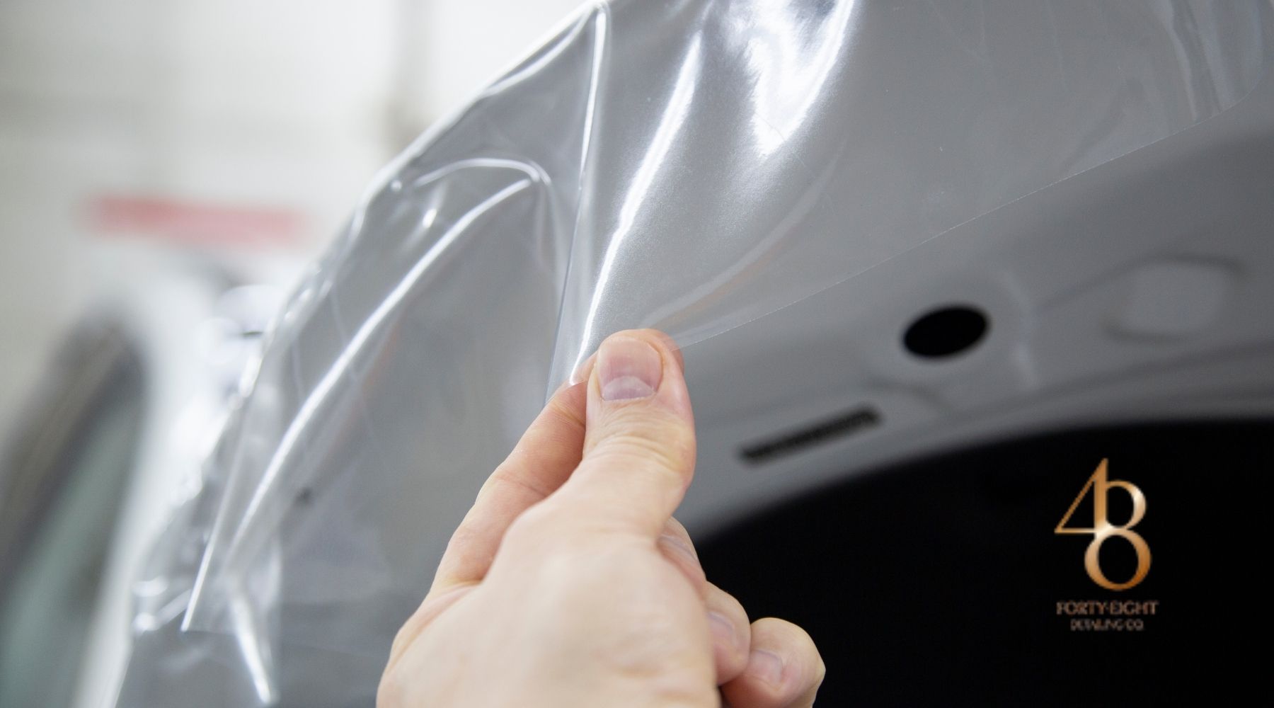 Hand applying clear paint protection film to a white Tesla panel at 48 Detailing