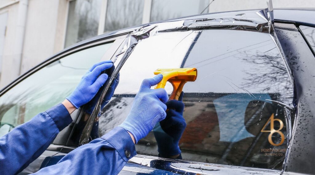Technician applying ceramic window tint film to a car side window