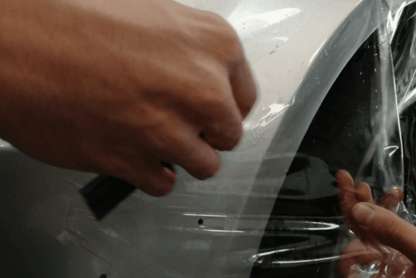 Close-up of paint protection film being applied to the front bumper of a white vehicle