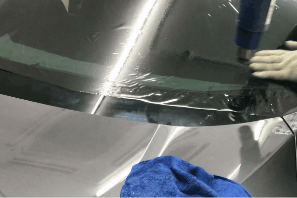 Technician heat shrinking window tint film onto a car windshield during installation