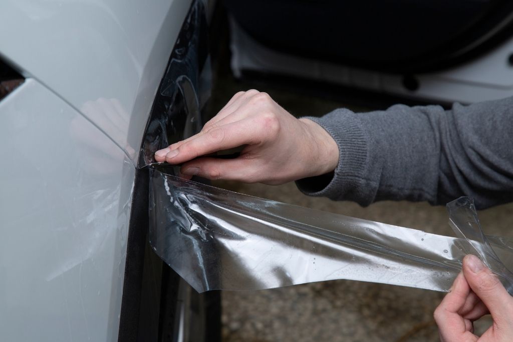 Technician applying clear paint protection film to the front fender area of a white Tesla