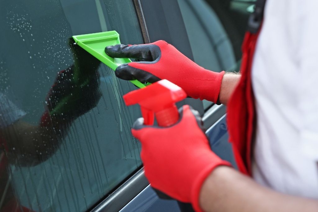 Technician smoothing window tint film onto a car side window with a squeegee