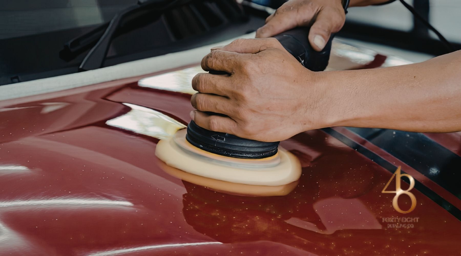 Technician polishing a red vehicle hood with a dual-action buffer during professional car detailing