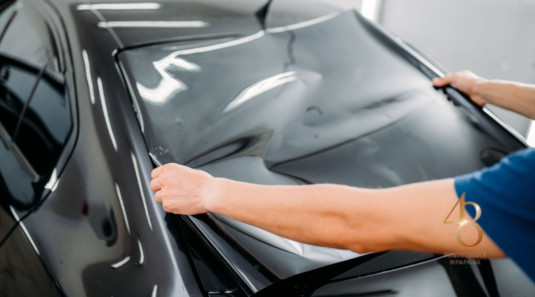 Technician applying ceramic window tint film to a car windshield in a professional auto detailing shop