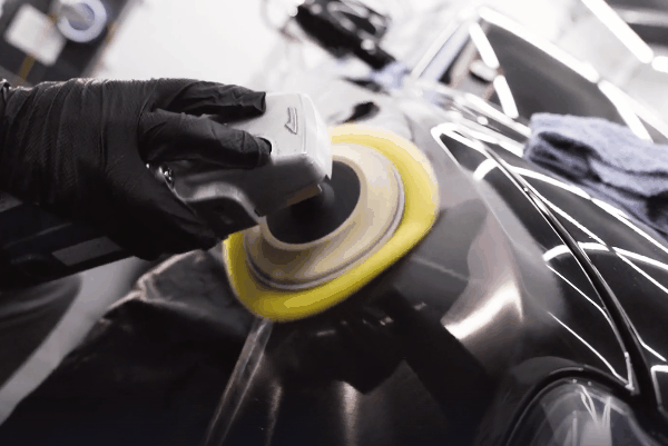 Technician polishing a black vehicle with a machine buffer during paint correction service