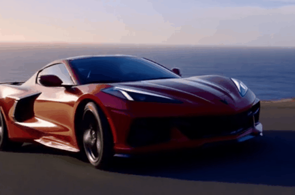 Red Corvette C8 driving on an open road with ocean view in the background during sunset