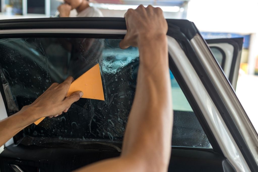 Technician applying window tint film to a car side window using a squeegee during professional installation
