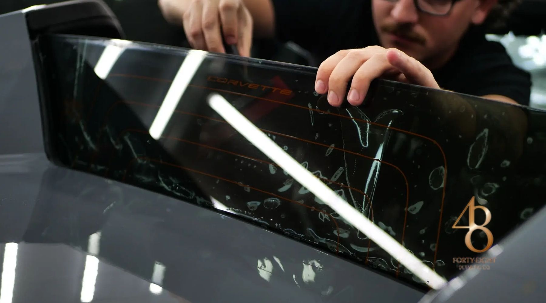 Technician installing ceramic window tint on a Corvette rear window at 48 Detailing.