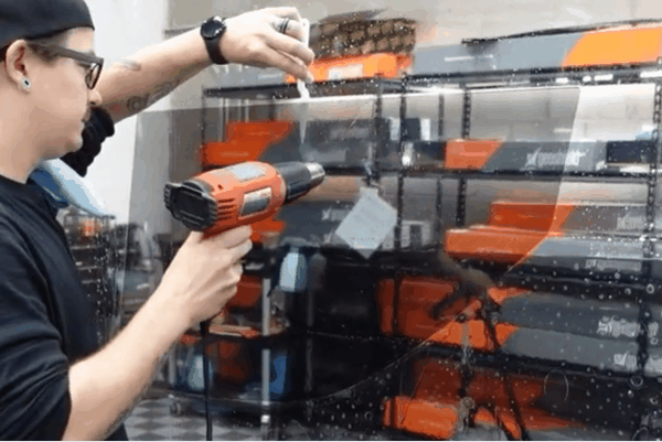 Technician heat shrinking automotive window tint film during professional installation.