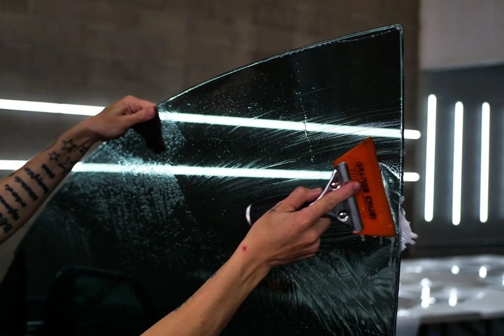 Technician applying automotive window tint film to a car window using a squeegee.