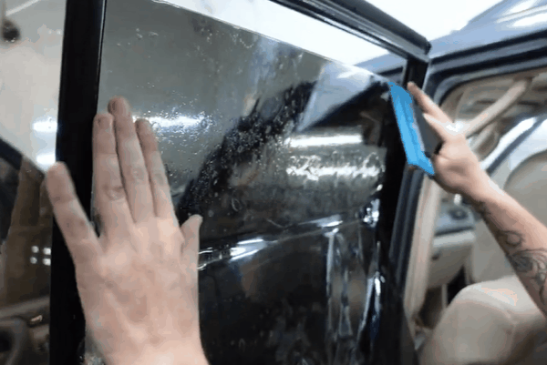 Technician smoothing window tint film onto a car door window with a squeegee