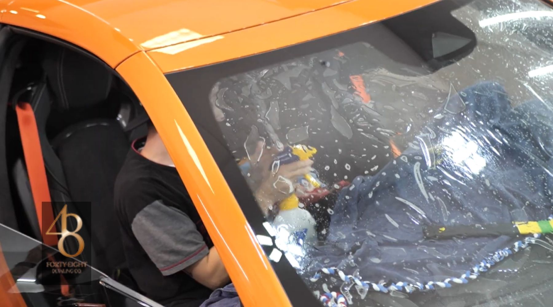 Technician installing window tint film on the windshield of an orange sports car at 48 Detailing.