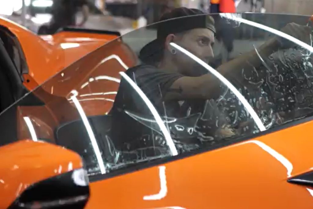 Technician applying window tint film to the side window of an orange sports car inside the 48 Detailing shop.