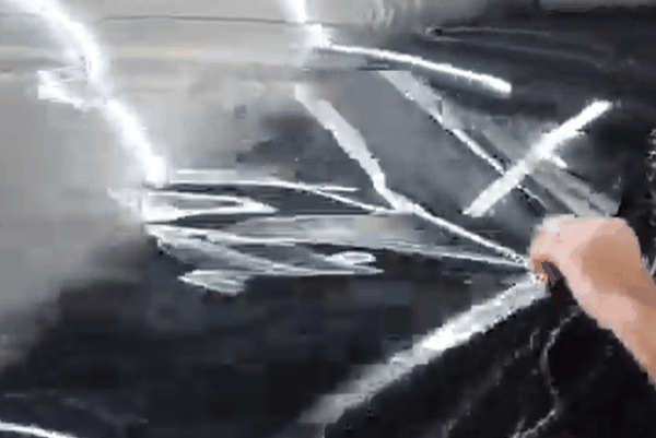 Close-up of a technician smoothing wet window tint film onto automotive glass with a squeegee.