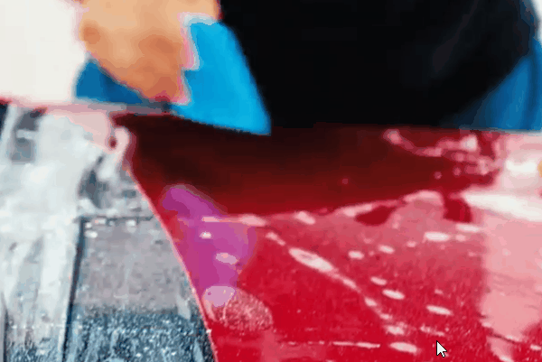 Technician smoothing clear paint protection film over the edge of a red vehicle panel during installation.