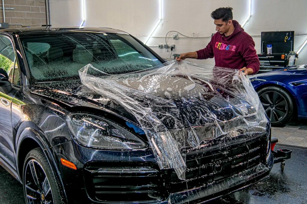 Technician applying paint protection film to the hood of a black SUV.