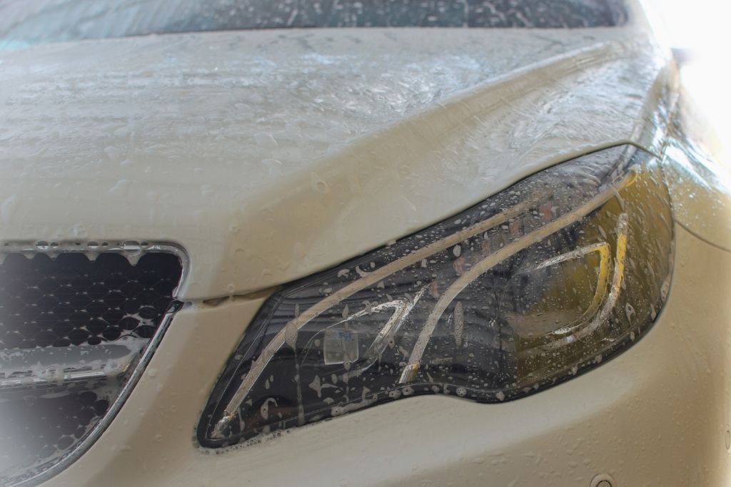 Close-up of a vehicle headlight and hood covered in soapy water during exterior detailing.