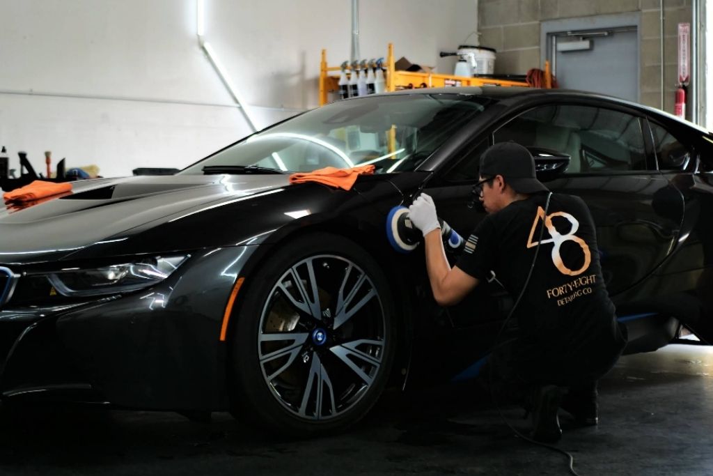 48 Detailing technician polishing the front fender of a black BMW inside a professional detailing studio.