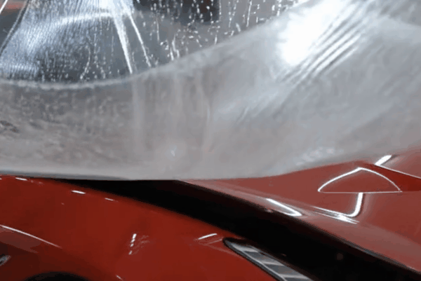 Paint protection film being applied to the hood of a red vehicle.