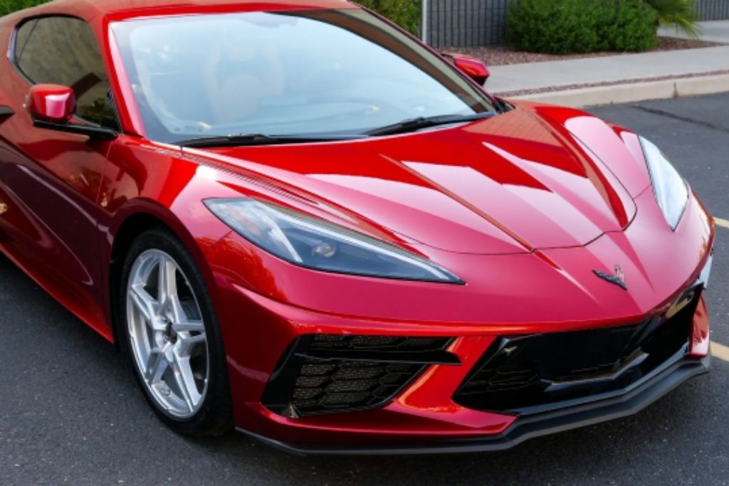 Red Corvette C8 parked outdoors with a glossy exterior finish, showcasing its low stance and sculpted front-end design.
