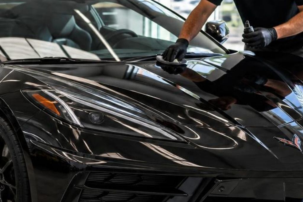 Technician applying ceramic coating to the hood of a black Corvette C8 to enhance gloss and surface protection.